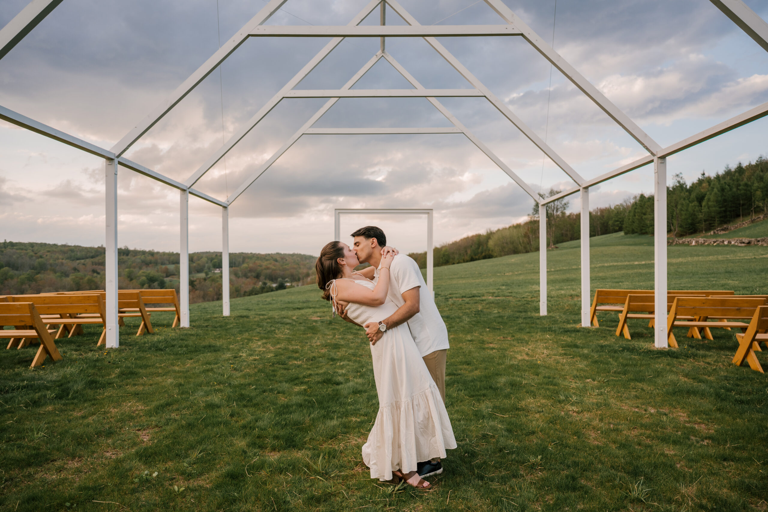 couple kissing under ceremonial archway for their engagement session at the venue at Carley brook