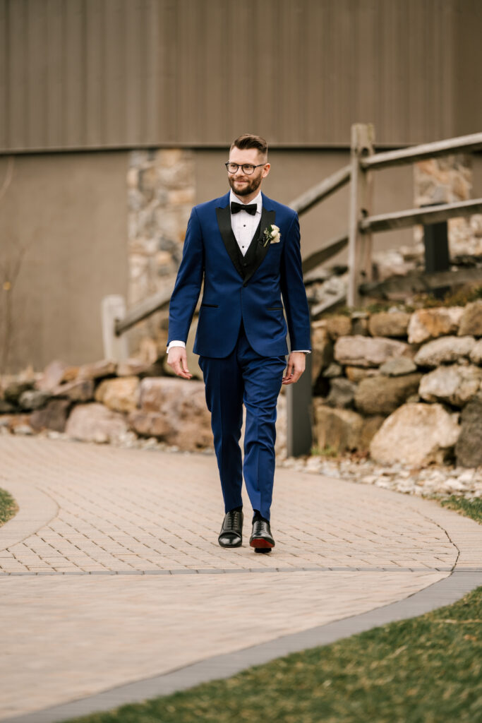 groom walking down the aisle in a navy blue suit with black details