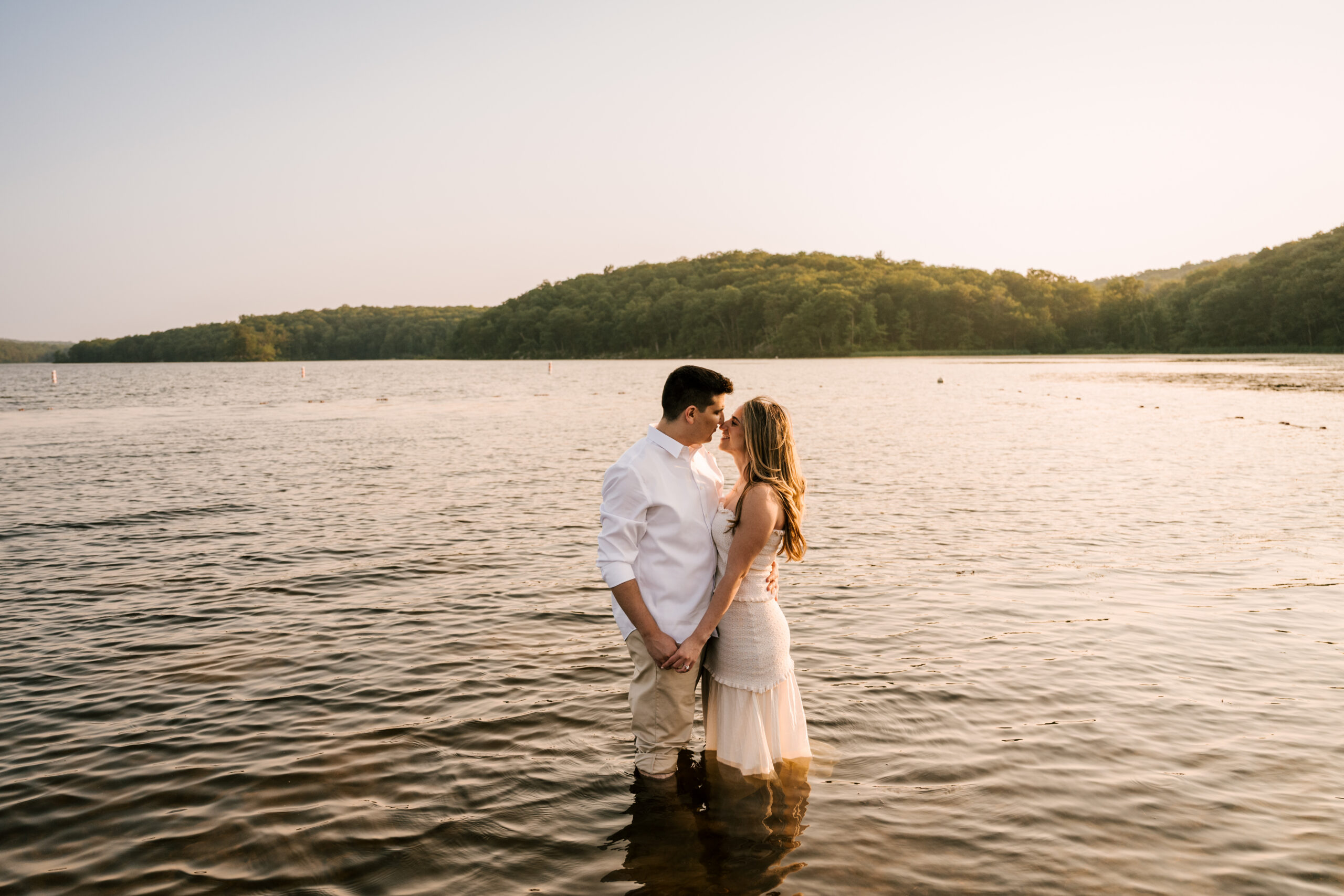 couple standing in the water with the golden hour light reflecting, holding hands and gazing into each other's eyes