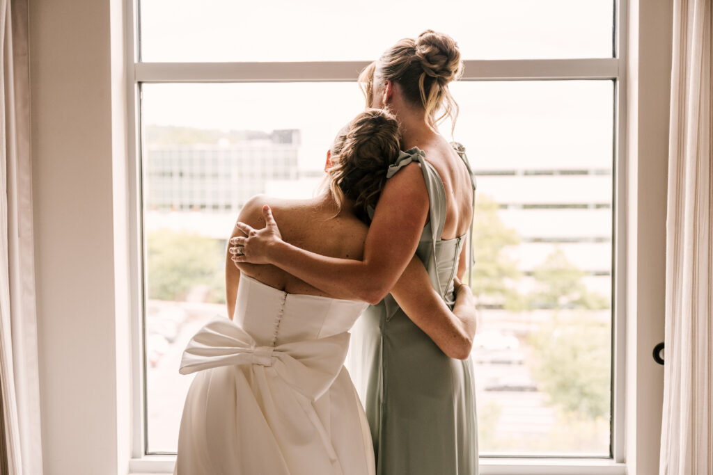 bride and her bridesmaid embracing and looking out the window while getting ready for first look at stone house at stirling ridge