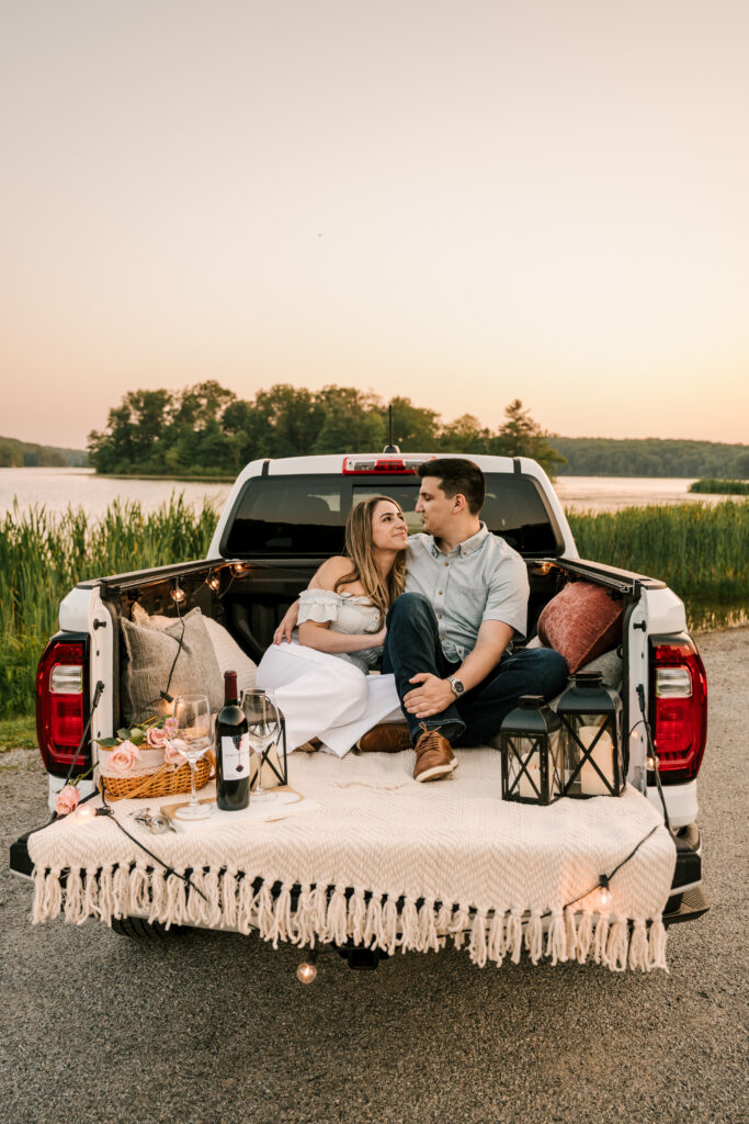 couple laying in back of truck with blankets and pillows, lanterns and wine