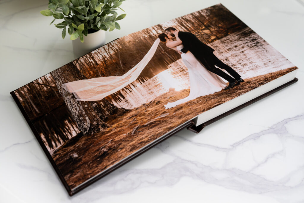 wedding album full page layout with bride and groom kissing in front of a lake and her veil floating behind her. 