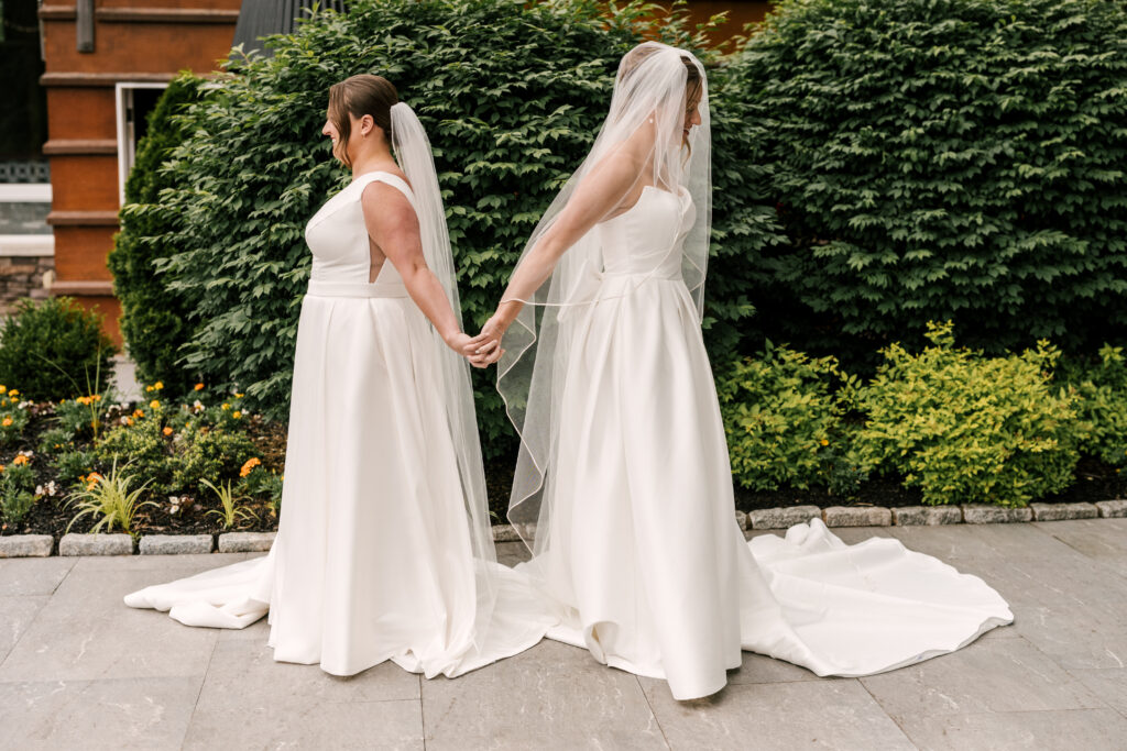 brides holding hands and back to back preparing for their first look at their nj may wedding