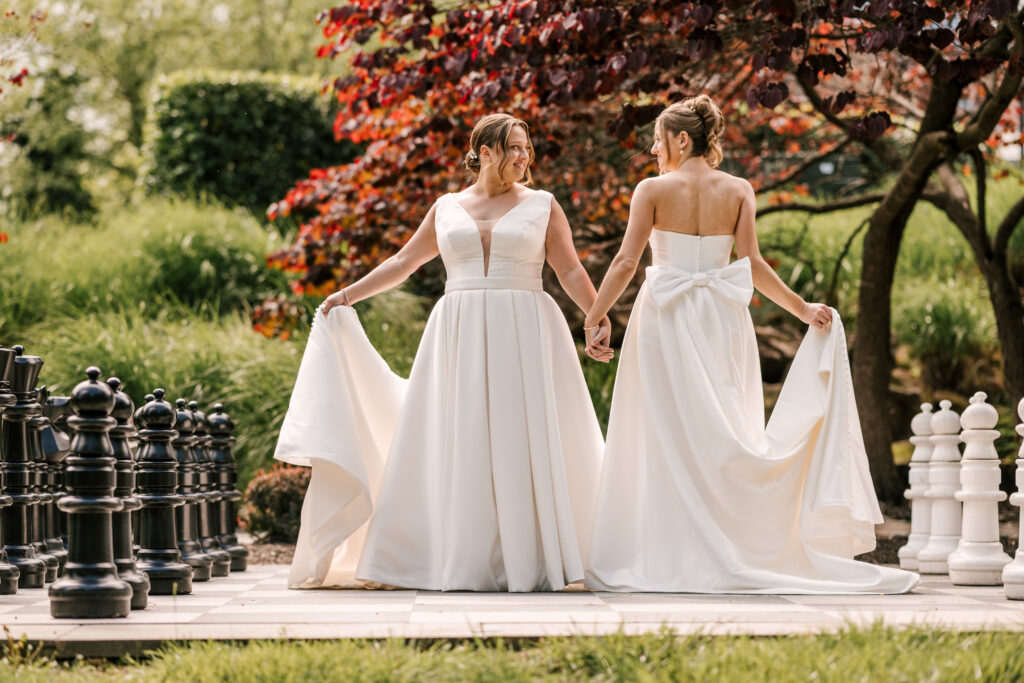 two brides holding hands and looking at one another standing on a giant chessboard at their wedding in nj