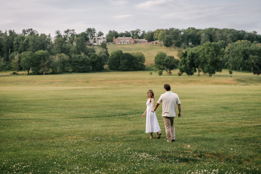 Engaged couple wanders the field at Natirar in Peapack, Gladstone NJ for their June engagement session. Mansion in the background