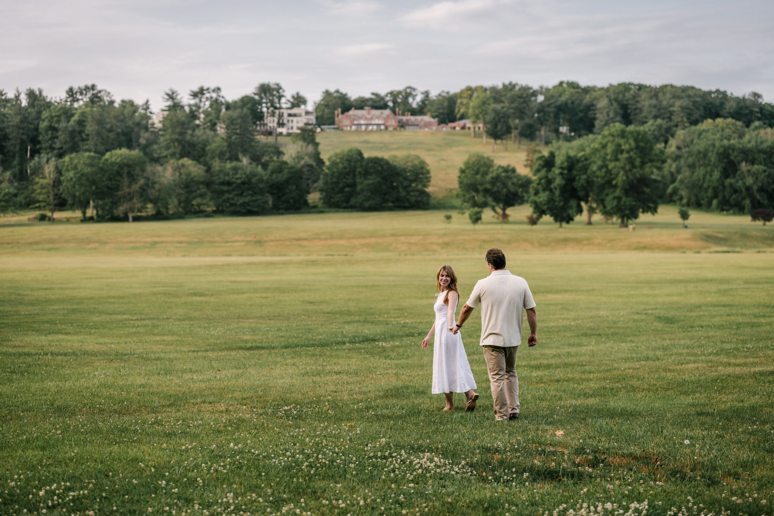 Engaged couple wanders the field at Natirar in Peapack, Gladstone NJ for their June engagement session. Mansion in the background